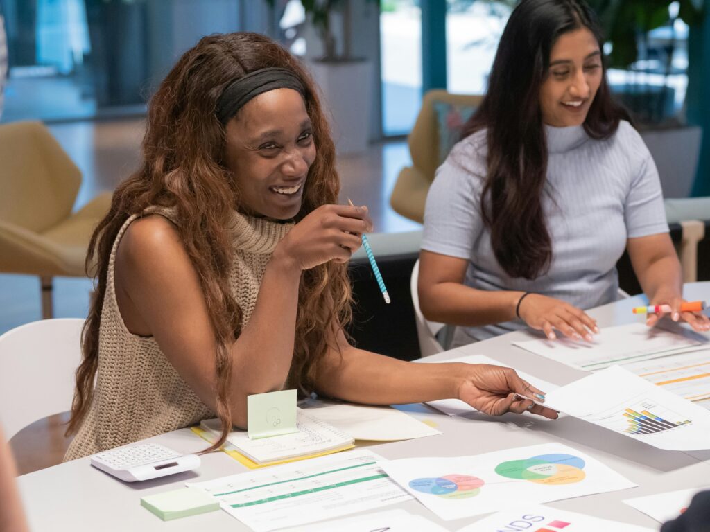Two women collaborating in a lively office meeting, exchanging ideas and smiling.